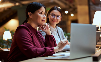 Duas profissionais trabalhando juntas em ambiente corporativo com laptop